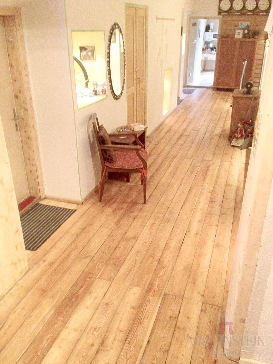 Langer Flur mit breiten Holzplanken, traditionellen Möbeln und Spiegeln an der Wand.