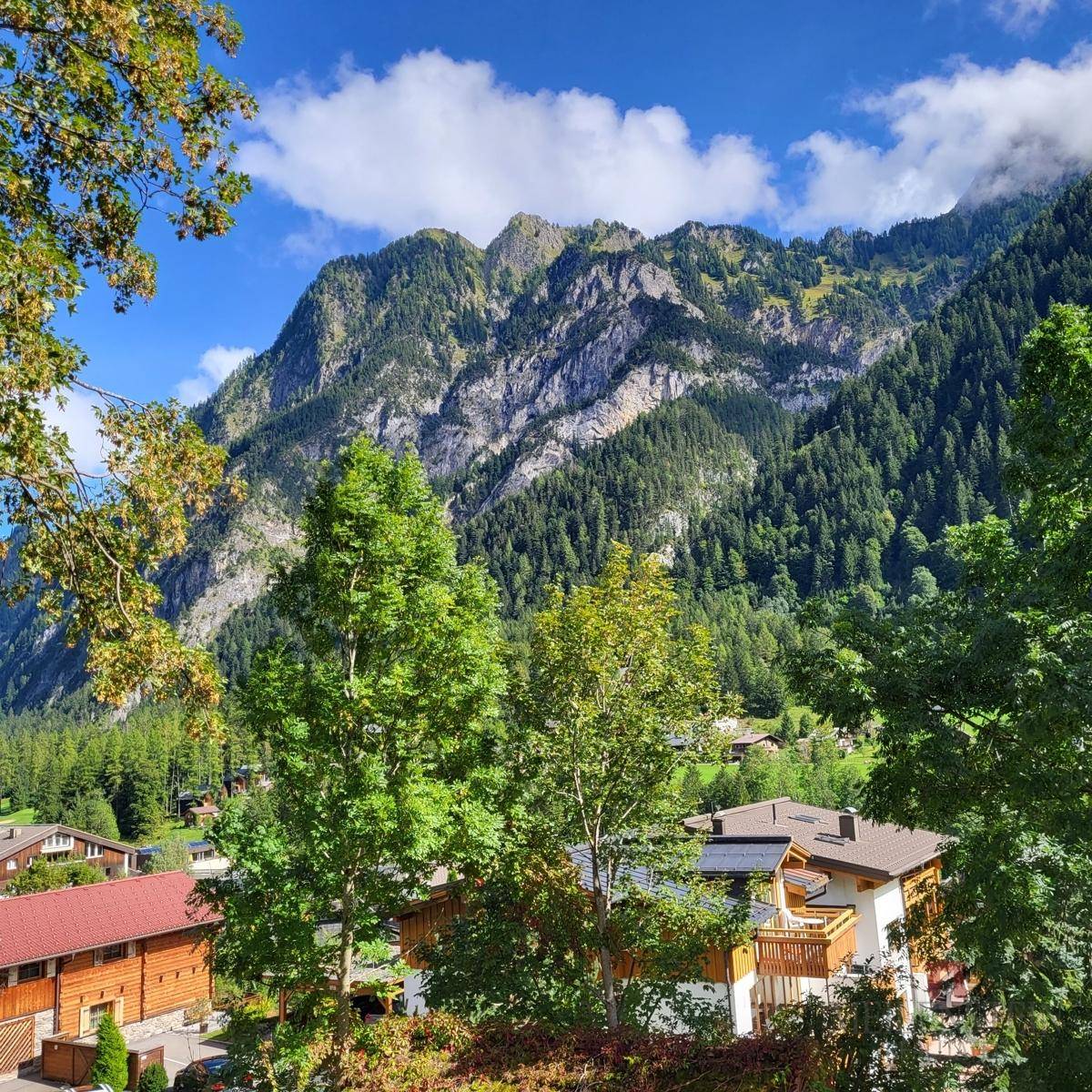 Atemberaubender Blick auf majestätische, bewaldete Berge und Häuser im Tal unter blauem Himmel.