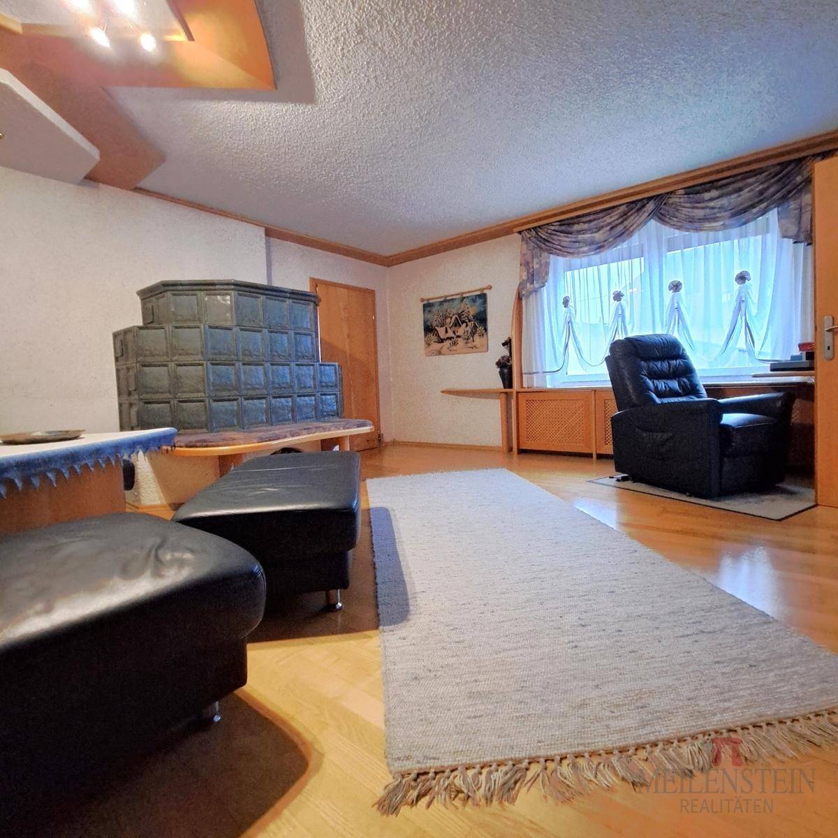 Gemütliches Wohnzimmer mit traditionellem Kachelofen, Holzboden und Sitzgelegenheiten.