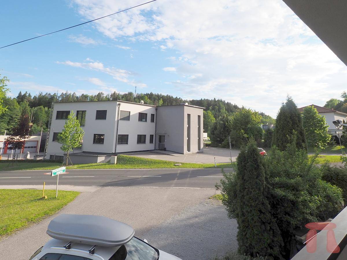 Blick von einem Balkon auf eine Straße, ein modernes Gebäude und grüne Hügel in der Ferne.
