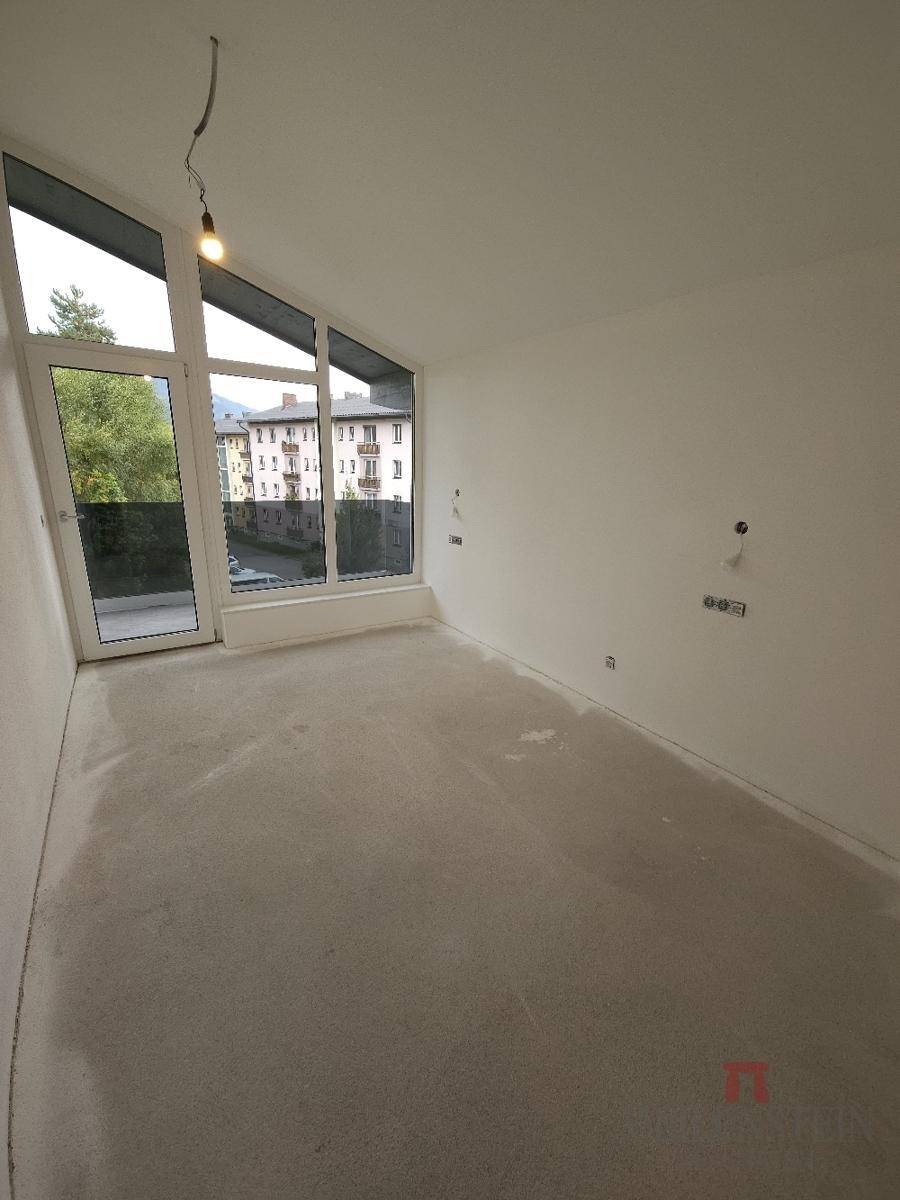 Helles, unfertiges Zimmer mit großen Fenstern und Rohbetonboden.