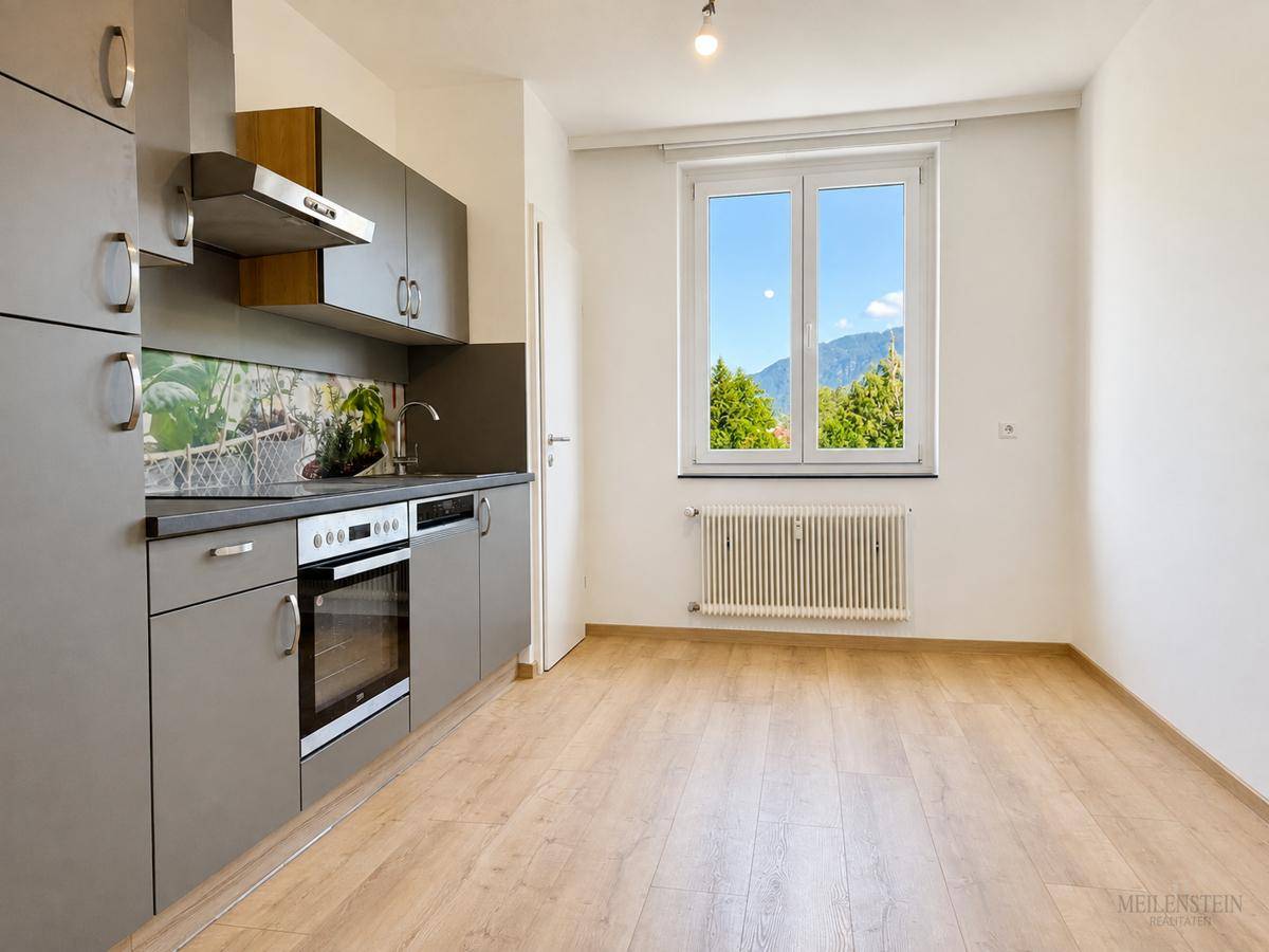 Helle Küche mit Fenster, das einen Blick auf die Berge bietet, und modernem Laminatboden.