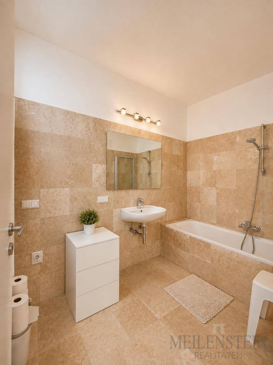 Helles Badezimmer mit beigefarbenen Fliesen, Badewanne mit Duschfunktion und modernem Waschbecken.