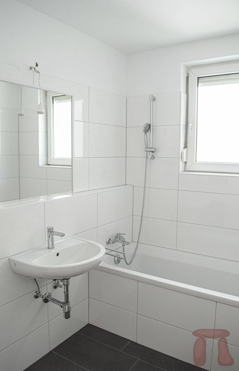 Modernes Badezimmer mit weißen Fliesen, Badewanne und Fenster für natürliche Belüftung.