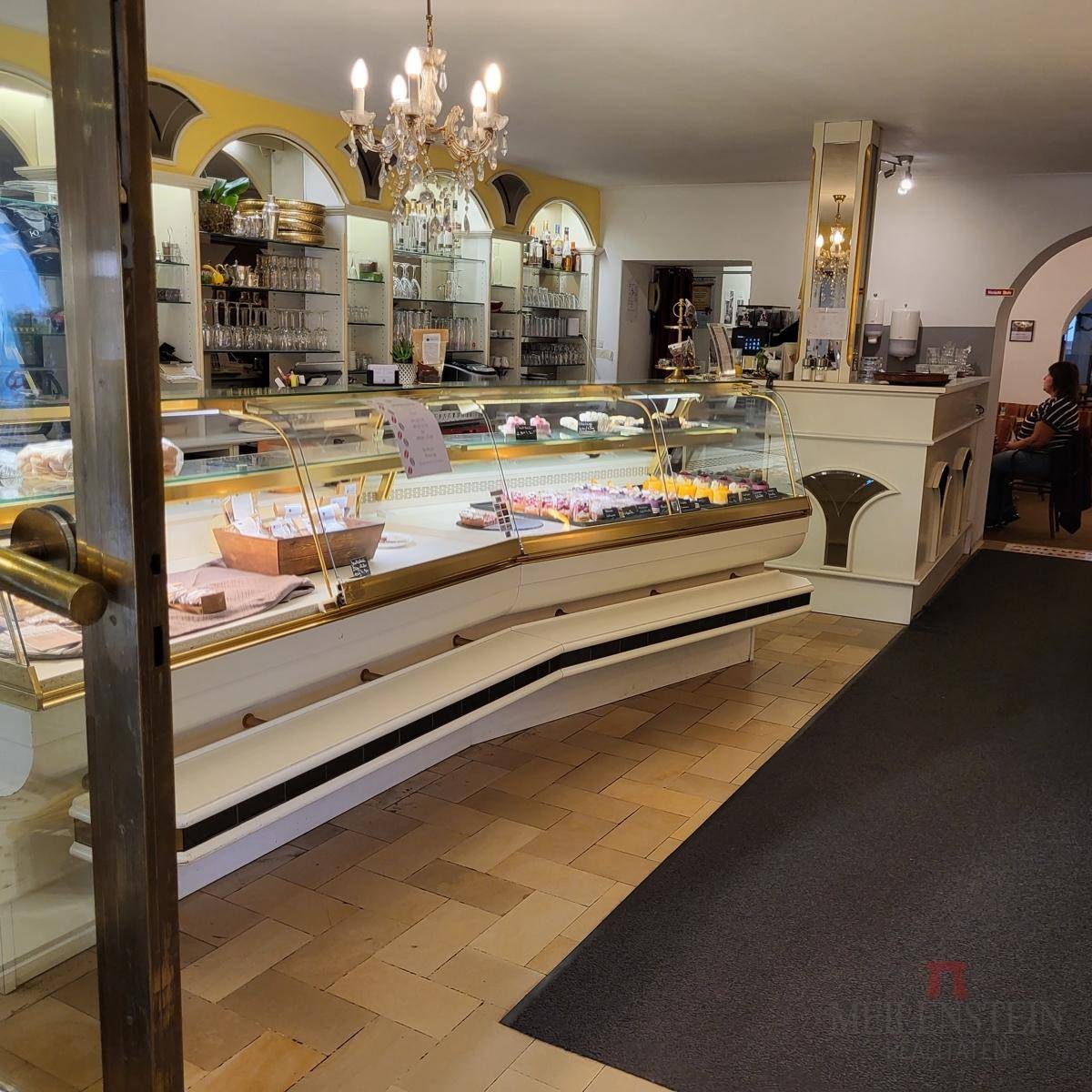 Innenansicht eines Cafés mit einer langen Theke voller Kuchen und Gebäck sowie einem Kronleuchter.
