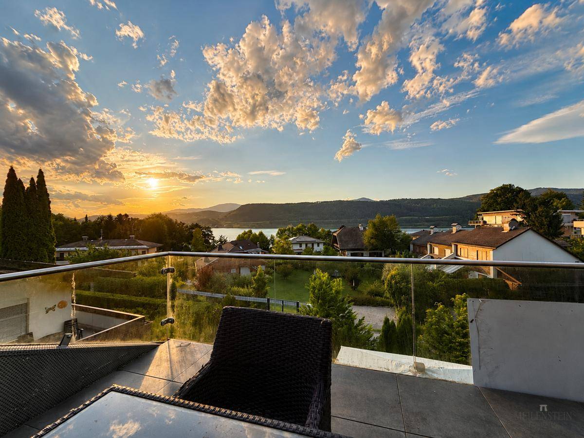 Gemütliche Terrasse mit Glasgeländer und Panoramablick auf den See und die malerische Landschaft bei Sonnenuntergang.