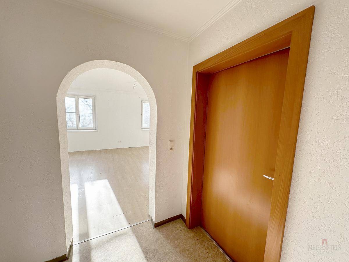 Flur mit Holztür und einem eleganten Rundbogen, der zu einem hellen Zimmer führt.
