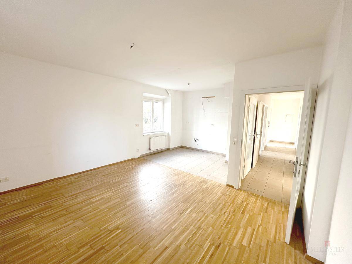 Heller Wohnbereich mit Parkettboden und einem offenen Durchgang zu einem angrenzenden Flur.