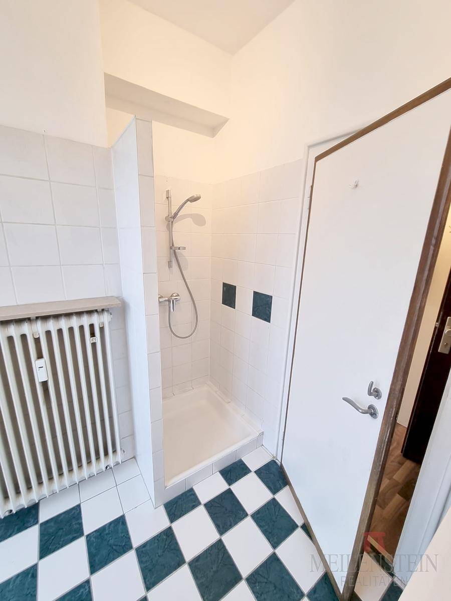 Badezimmer mit Duschbereich, Heizkörper und auffälligem Schachbrettmuster auf dem Fliesenboden.