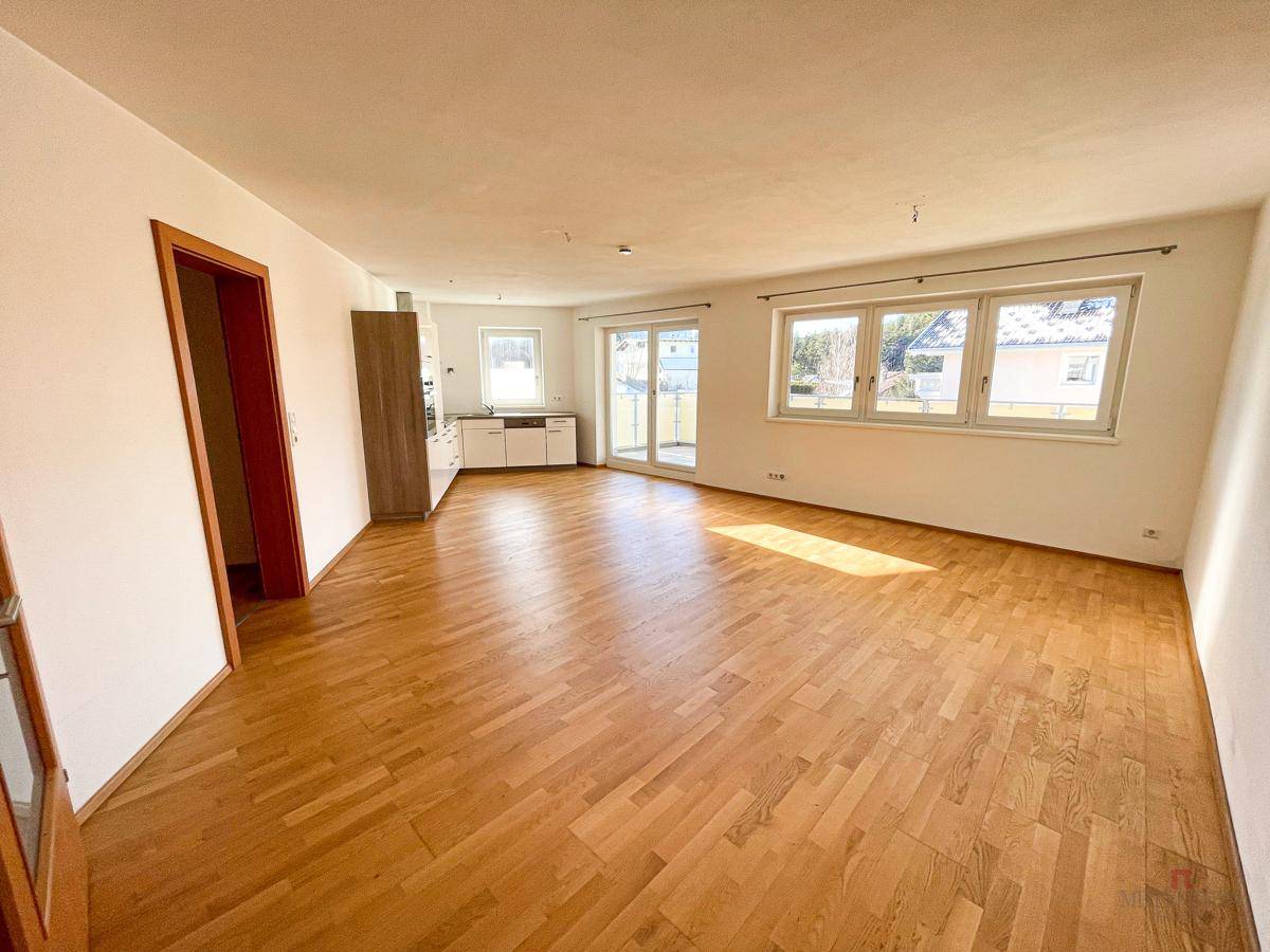 Heller, offener Wohnbereich mit Parkettboden, großen Fenstern und Zugang zu einem Balkon oder einer Terrasse.