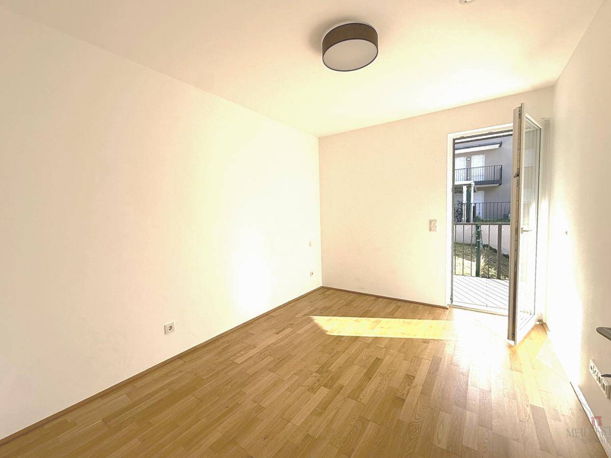 Helles Zimmer mit Parkettboden und direktem Zugang zu einem kleinen Gartenbereich oder Balkon.