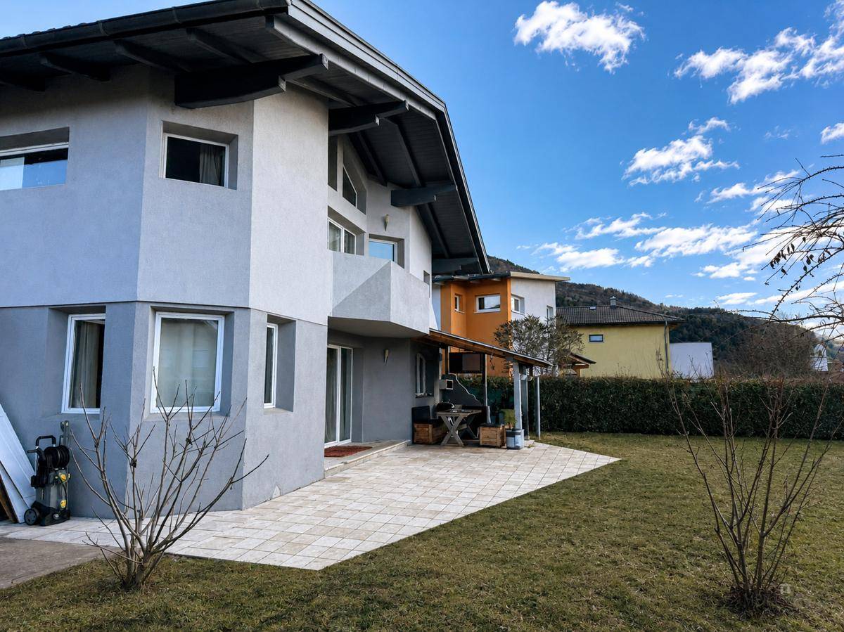 Gepflasterte Terrasse mit Überdachung und Sitzgelegenheiten, umgeben von einem gepflegten Garten.