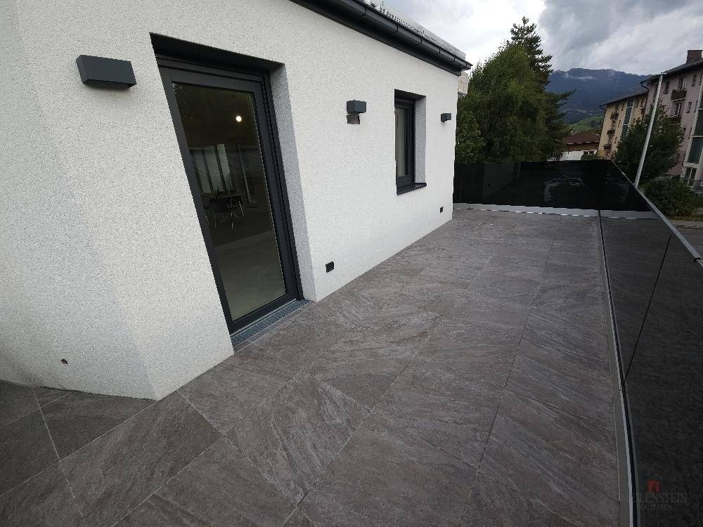 Moderne, geflieste Terrasse mit Glasbrüstung und Zugang zum Innenbereich.