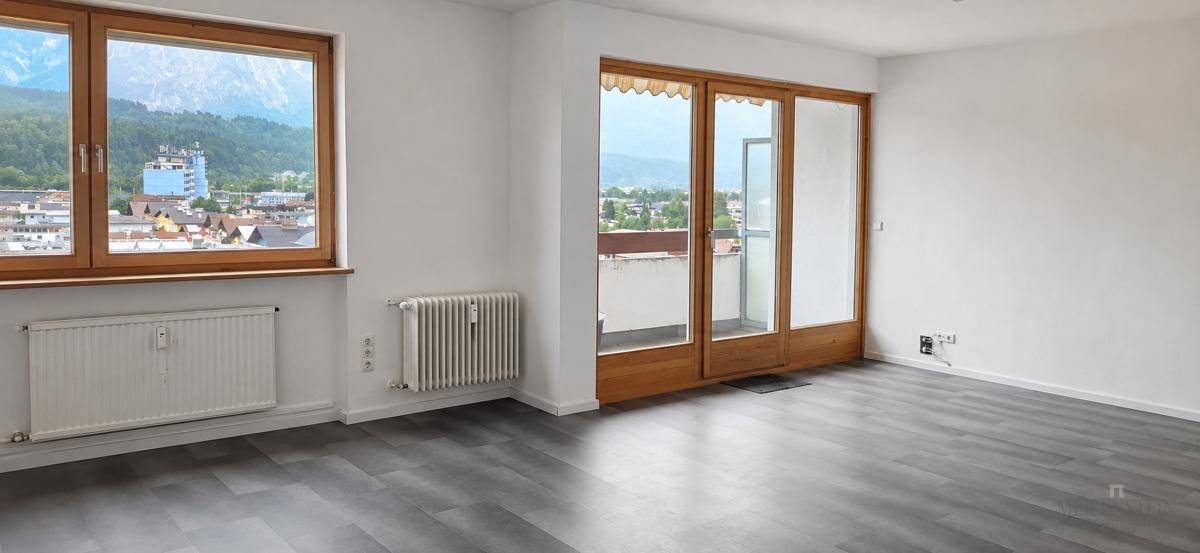 Heller Wohnraum mit modernem Laminatboden, großen Fenstern und Zugang zu einem Balkon mit Bergblick.