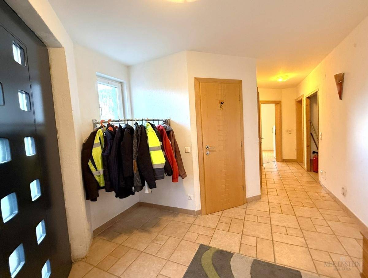 Heller Eingangsbereich mit Fliesenboden und Garderobe, der zu weiteren Räumen führt.