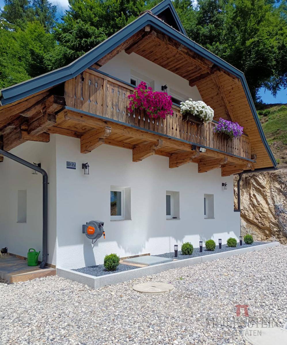 Balkon mit bunten Blumenkästen an einem charmanten Haus mit weißer Fassade und Holzelementen.