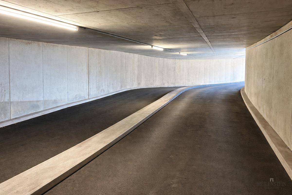 Geschwungene Zufahrtsrampe in einer Tiefgarage mit glatten Betonwänden und Deckenbeleuchtung.