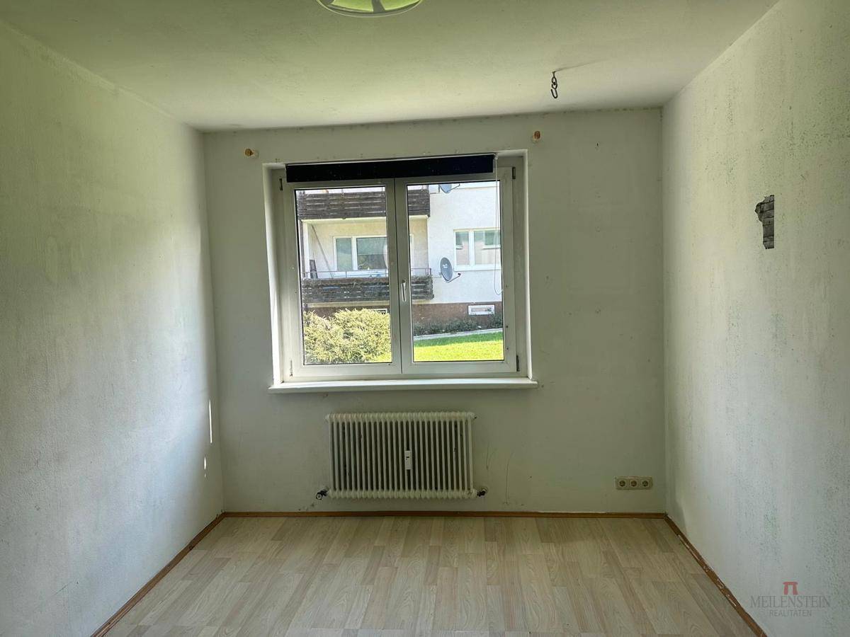 Leeres Zimmer mit Holzboden und Fenster, das auf eine Renovierung wartet.