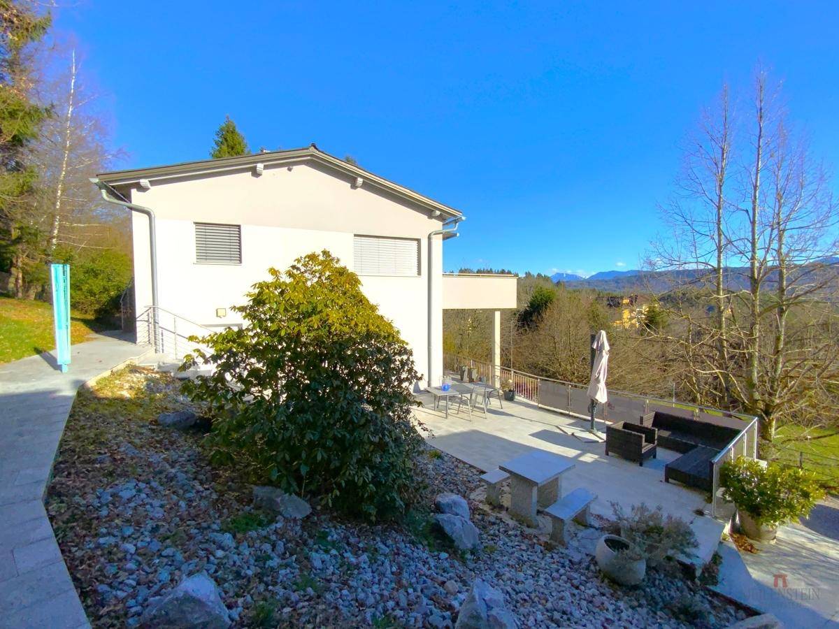 Große gepflasterte Terrasse mit verschiedenen Sitzbereichen und Blick auf die grüne Umgebung.