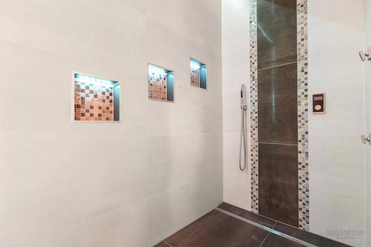 Geräumige Dusche mit modernen Fliesen, Mosaikakzenten und integrierten Nischen.
