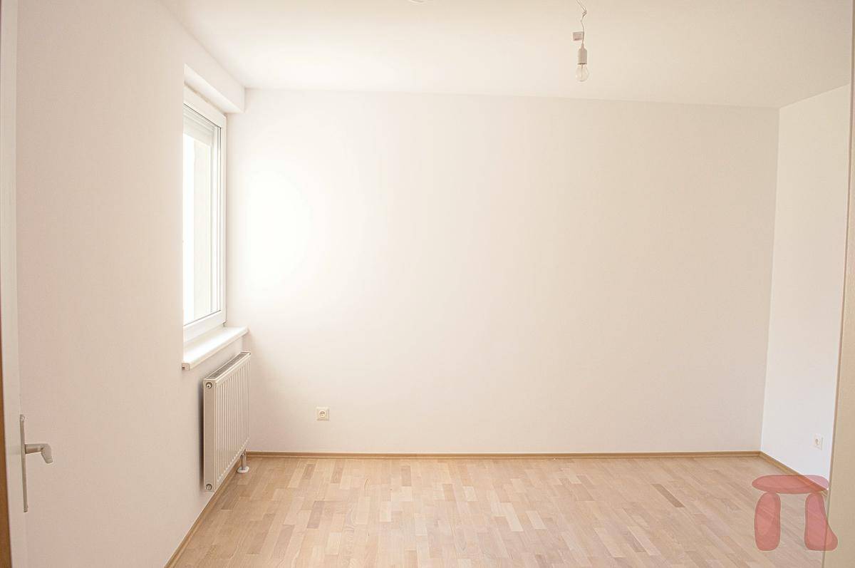 Helles Schlafzimmer mit Parkettboden und einem Fenster, das viel natürliches Licht bietet.