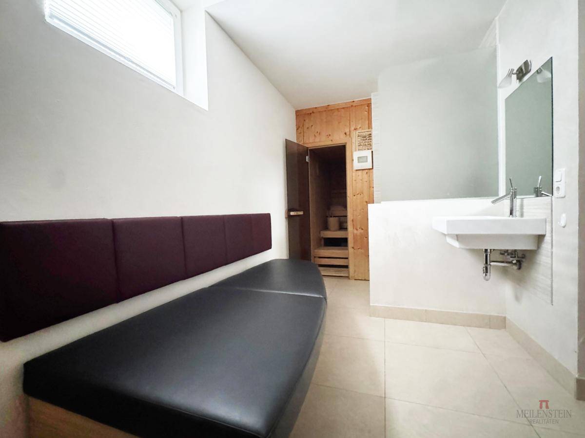 Entspannungsbereich mit Liege, Waschbecken und Zugang zur Sauna, hell und funktional.