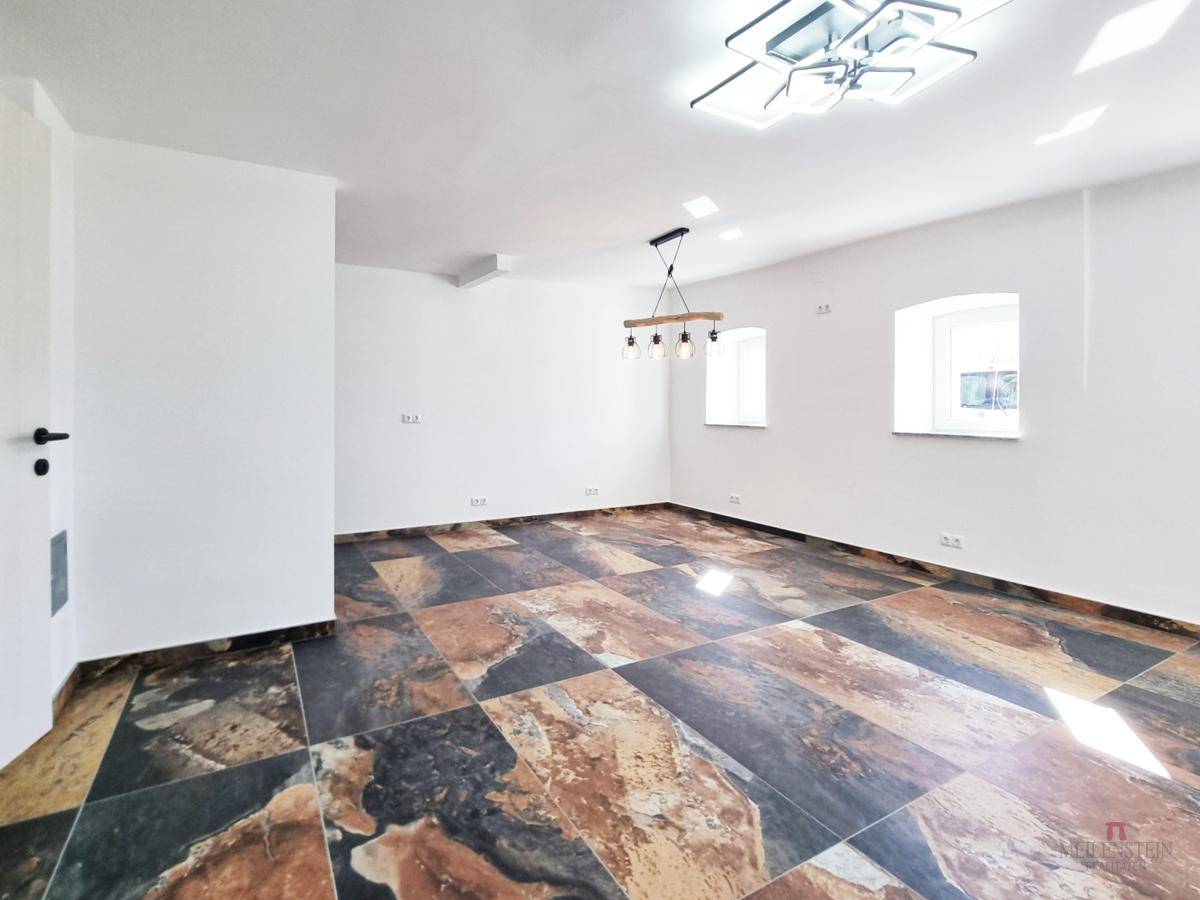 Heller Raum mit auffälligem Fliesenboden in verschiedenen Brauntönen und kleinen Fenstern.