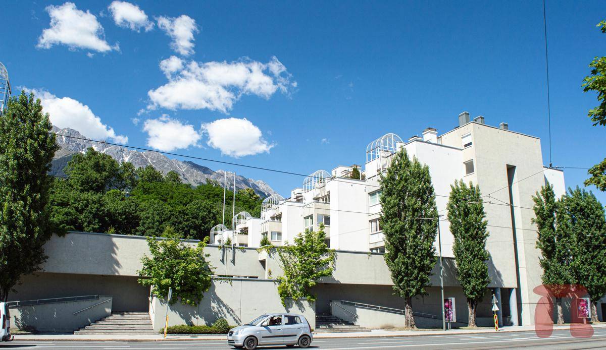 Straßenansicht des Wohnkomplexes mit Bäumen und beeindruckendem Bergpanorama im Hintergrund.