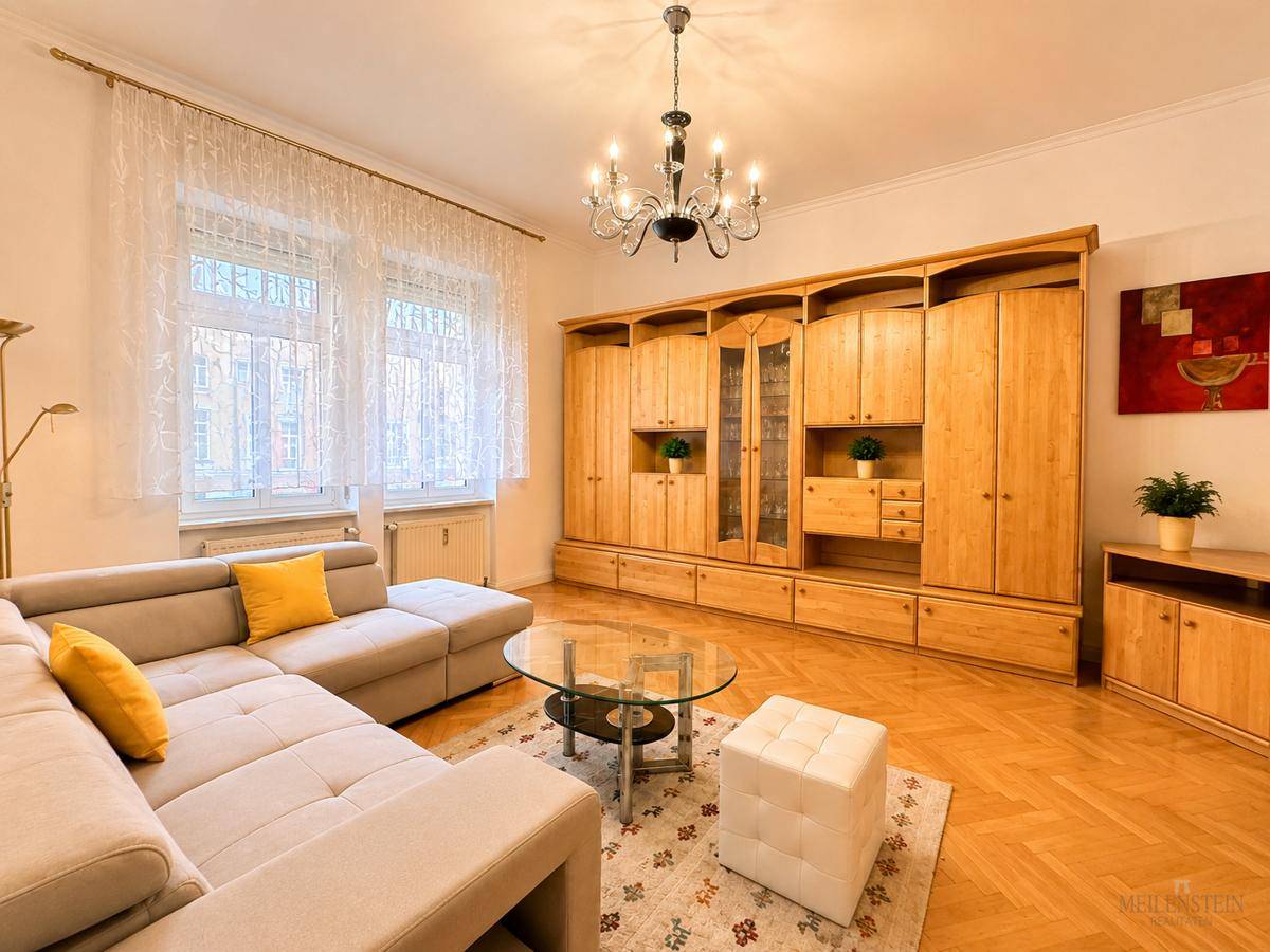 Detailansicht des Wohnzimmers mit großer Holzschrankwand und Fenster mit Vorhängen.