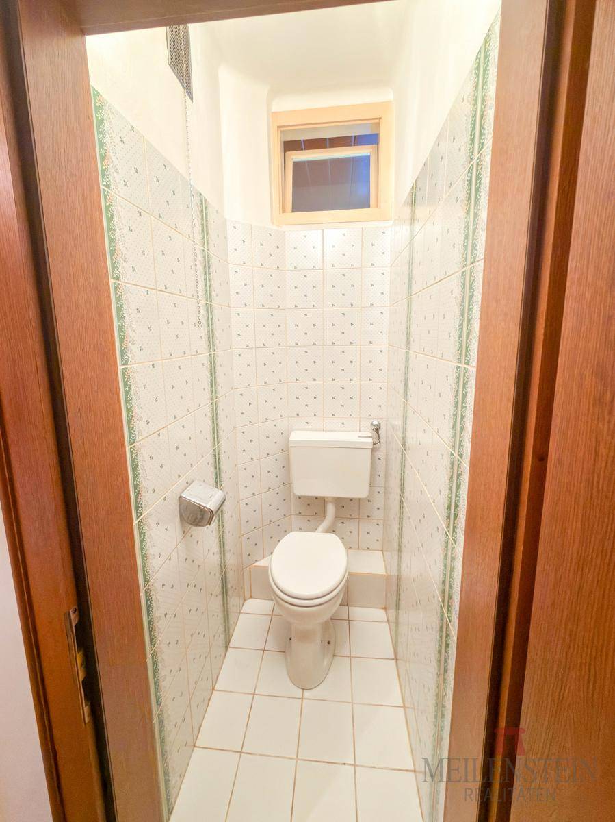 Kleines Gäste-WC mit Fliesen an den Wänden und einem Fenster für natürliche Belüftung.
