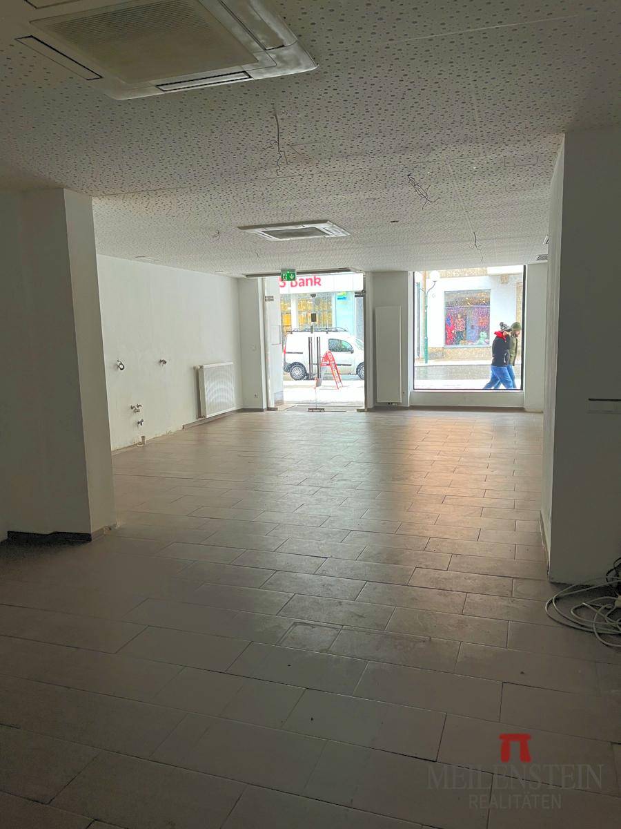 Leerer Gewerberaum mit Fliesenboden, Klimaanlage und großen Schaufenstern zur Straße hin.