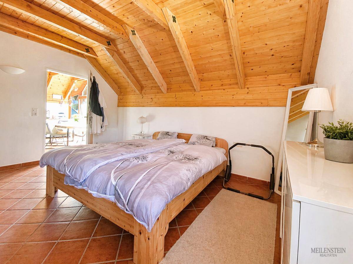 Schlafzimmer mit Holzbalkendecke, Doppelbett und Zugang zu einem weiteren Raum.
