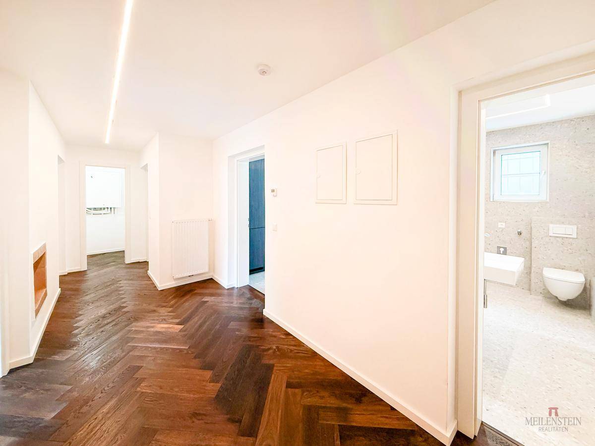 Langer Flur mit Fischgrätparkettboden und Blick in ein modernes Badezimmer.