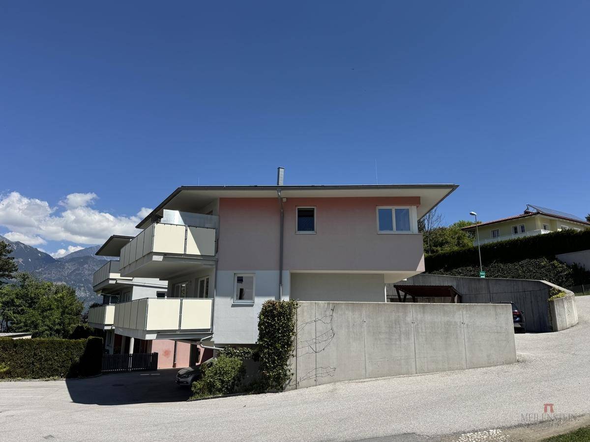 Modernes Mehrfamilienhaus mit Balkonen und Blick auf die umliegende Berglandschaft.