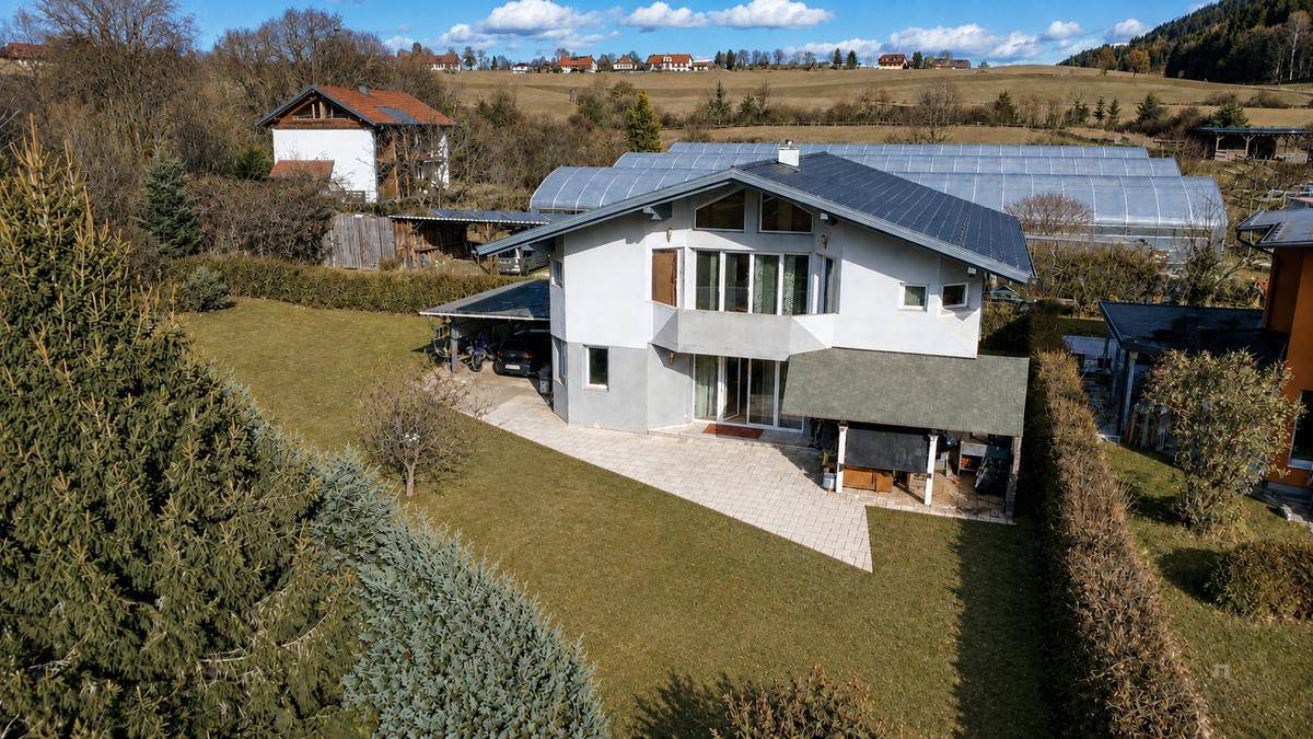 Luftaufnahme eines Einfamilienhauses mit Garten, Carport und gepflastertem Bereich in ländlicher Umgebung.