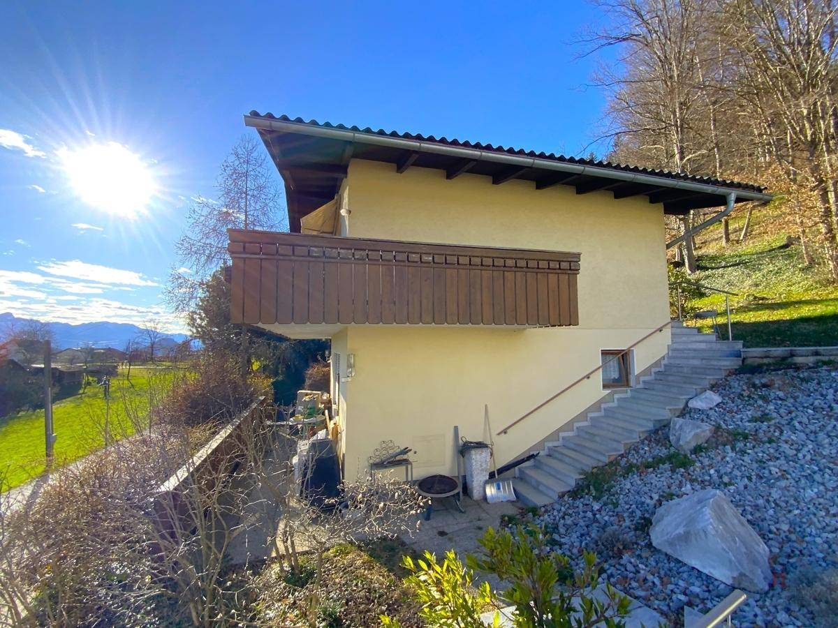 Seitenansicht eines traditionellen Hauses mit Holzbalkon und Treppenzugang im Sonnenlicht.