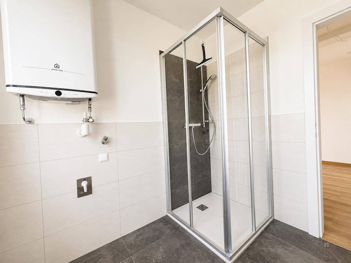 Modernes Badezimmer mit Duschkabine, weißen Fliesen und einem Warmwasserboiler.