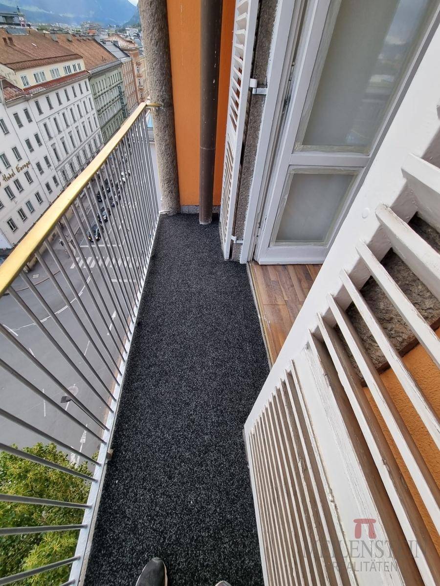 Schmaler Balkon mit Teppichboden und Blick auf die darunterliegende Straße und Gebäude.