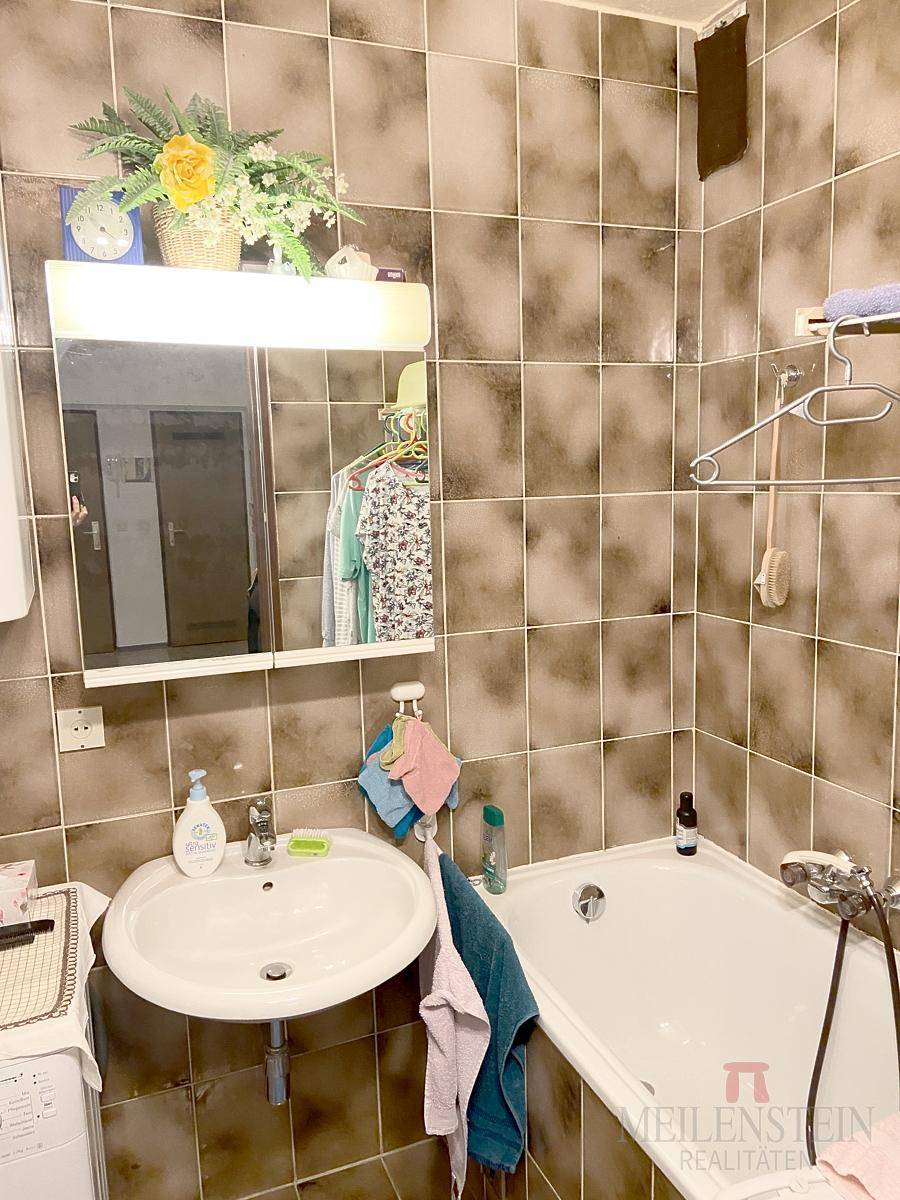 Badezimmer mit Badewanne, Waschbecken und braunen Fliesen, ausgestattet mit einem praktischen Spiegelschrank.
