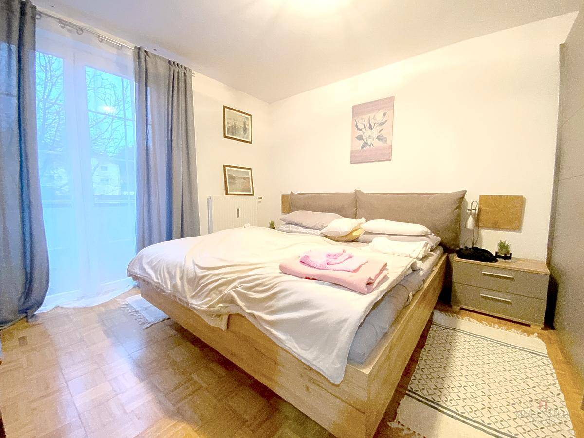 Helles Schlafzimmer mit Holzbett, Parkettboden und Zugang zu einem Balkon oder einer Terrasse.