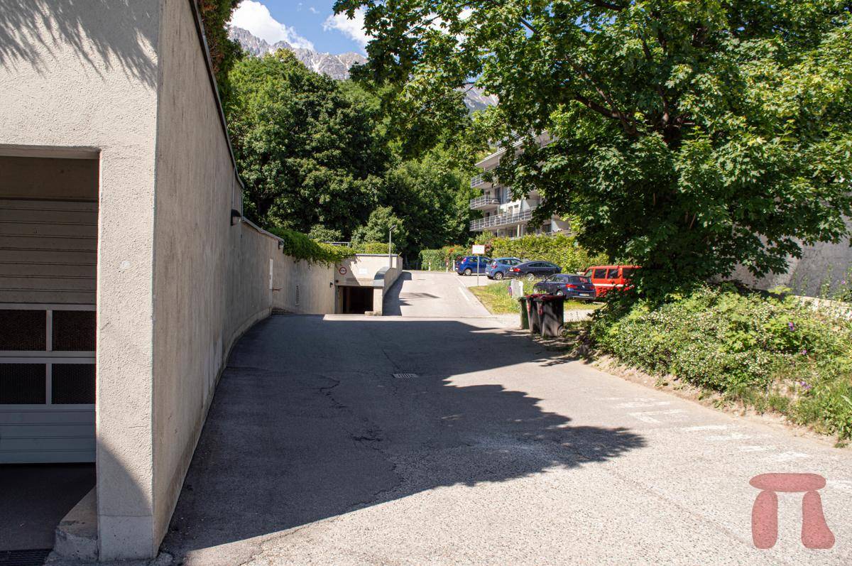 Zufahrt zur Tiefgarage des Wohngebäudes, umgeben von Bäumen und Grünflächen an einem sonnigen Tag.