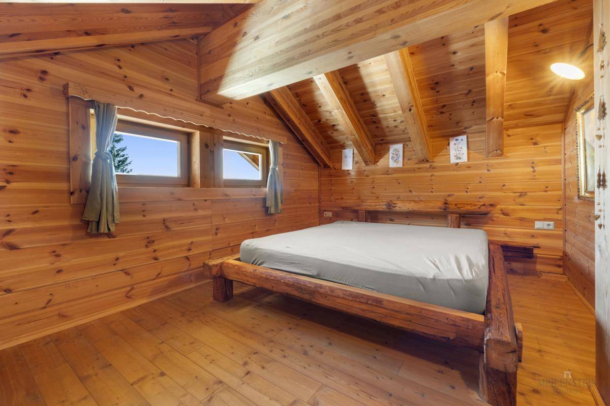 Helles Schlafzimmer mit Holzvertäfelung, Holzbett und schrägen Decken.