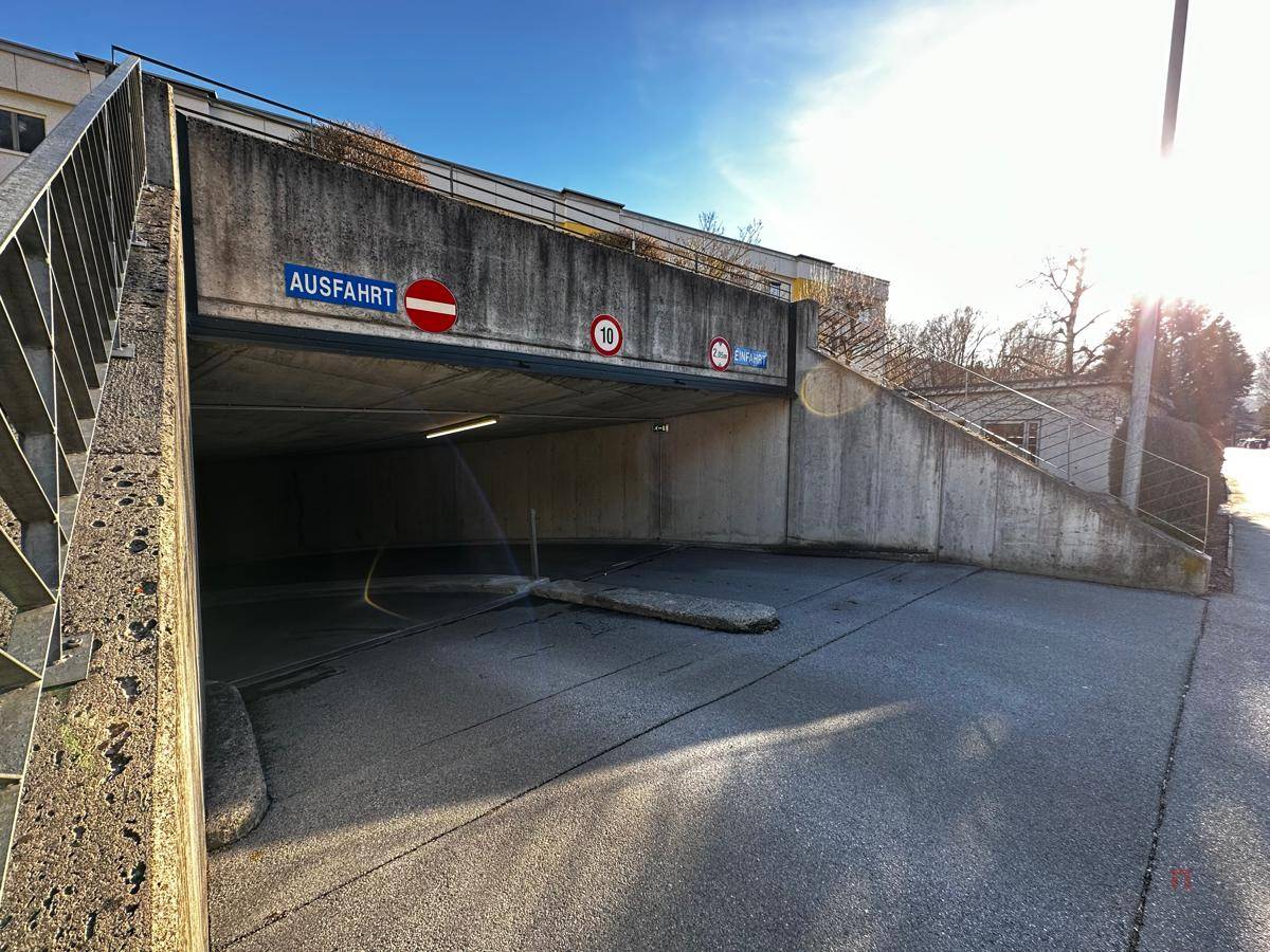Nahaufnahme der Einfahrt zur Tiefgarage mit Beschilderung und Betonwänden unter blauem Himmel.
