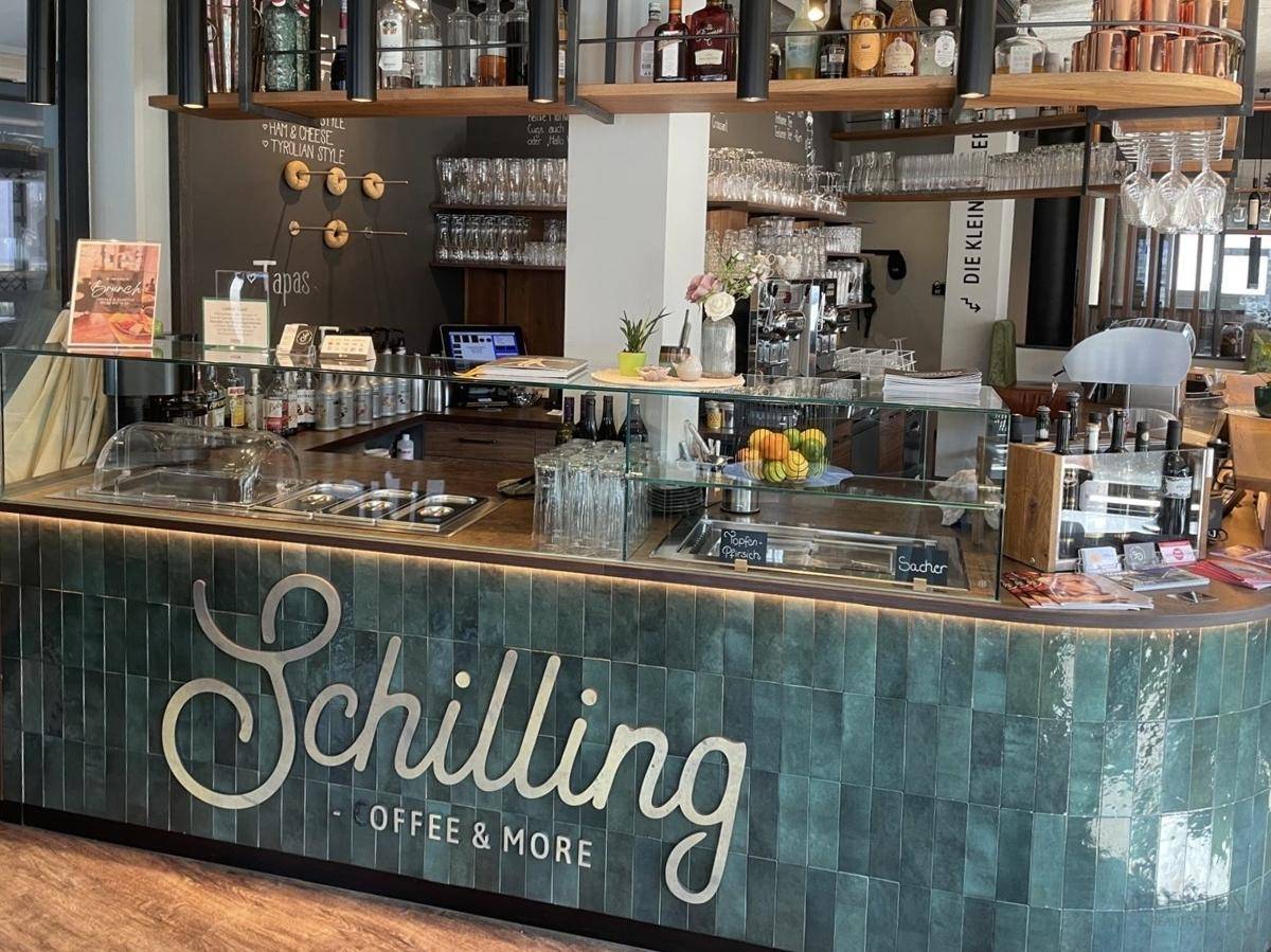 Die Theke der Bar mit grünen Fliesen, integriertem Logo und Auslage für Getränke und Speisen.
