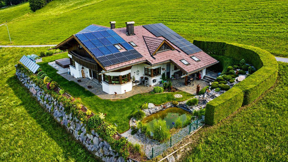 Luftaufnahme eines Hauses mit Solaranlagen, umgeben von einem gepflegten Garten mit Teich und Hecke.