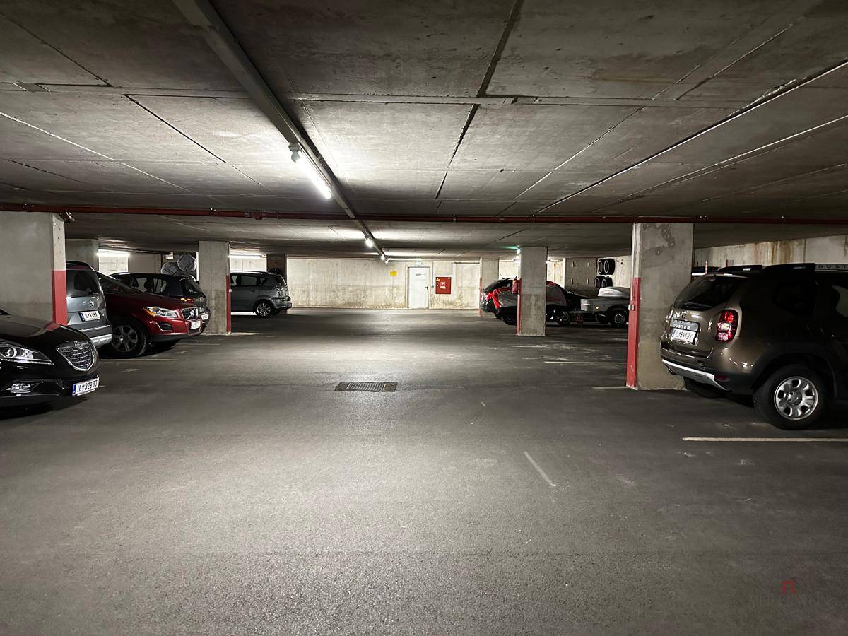 Weitläufige Tiefgarage mit zahlreichen geparkten Fahrzeugen und Betonpfeilern, gut beleuchtet.