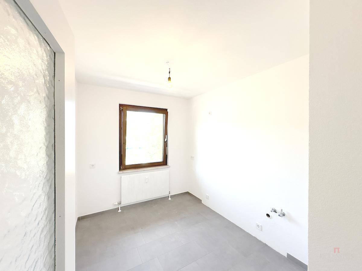 Funktionaler Raum mit grauen Fliesen, Fenster und Anschlüssen für Sanitärinstallationen.