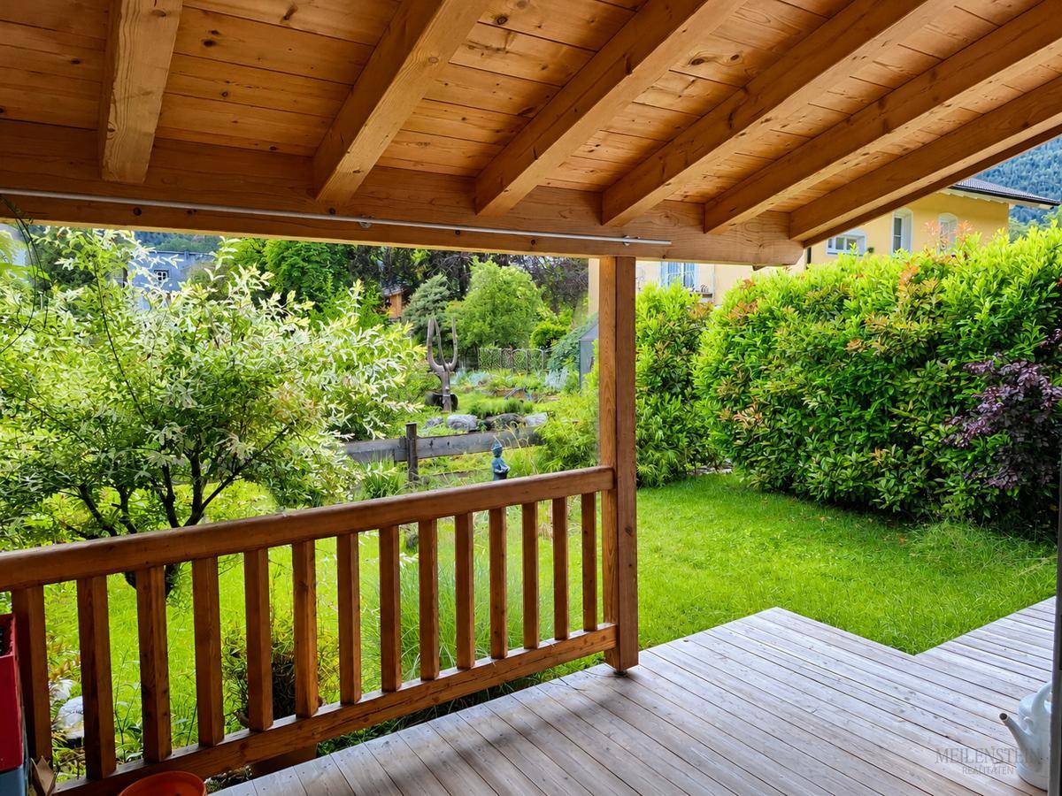 Blick vom überdachten Außenbereich in den grünen Garten mit Hecke und Bäumen.