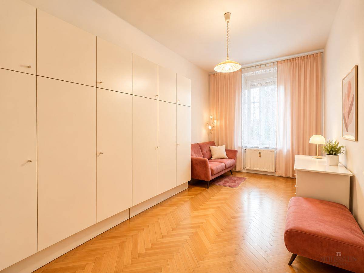 Zimmer mit Einbauschränken, rotem Sofa und Fischgrätparkettboden.