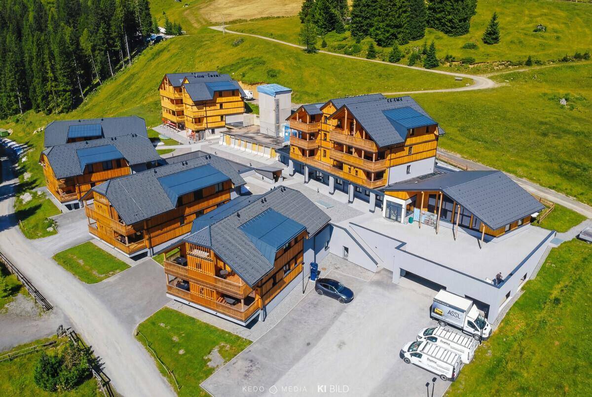 Vogelperspektive einer Wohnanlage mit mehreren Gebäuden im alpinen Stil, umgeben von Natur.